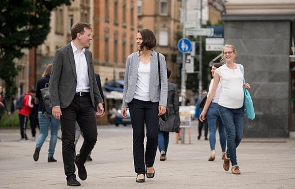 Drei Menschen laufen einander zugewandt durch eine Fußgängerzone