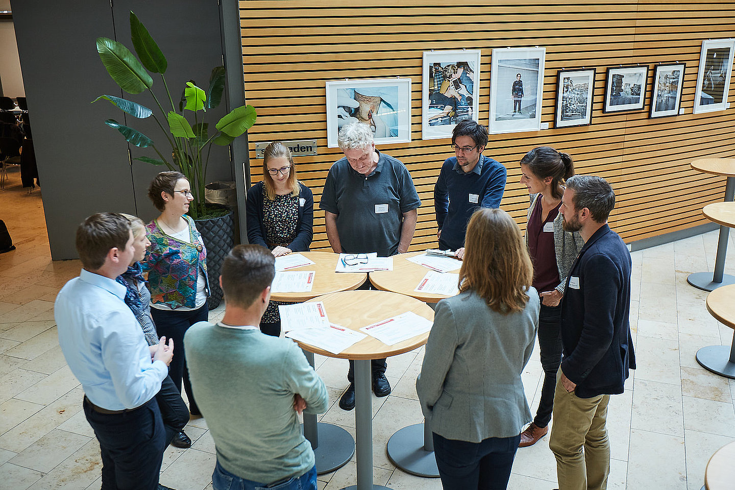 Eine Gruppe Menschen steht im Kreis um einen Tisch und diskutiert