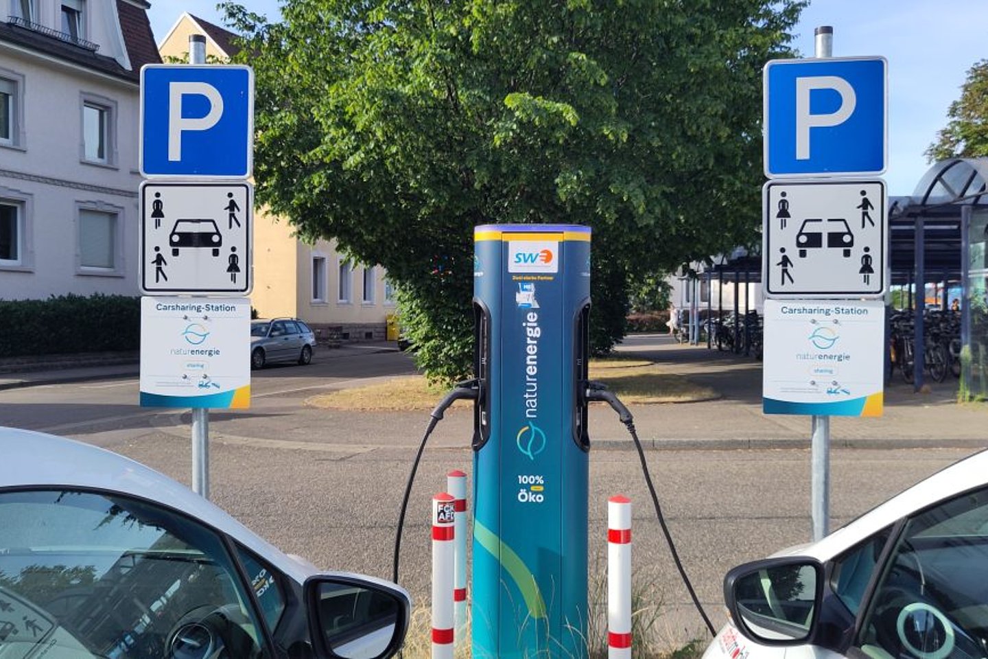 E-Ladesäule mit zwei ladenden Fahrzeugen und Verkehrsschildern