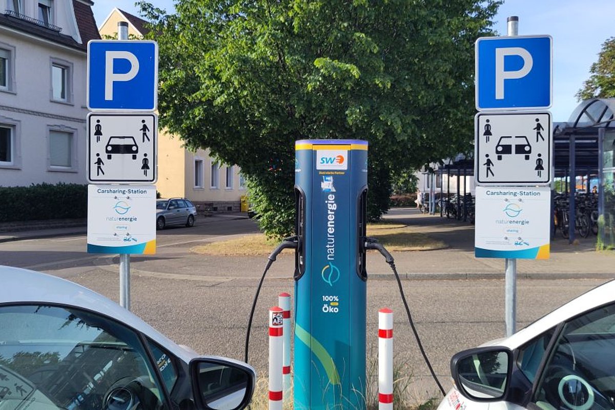 E-Ladesäule mit zwei ladenden Fahrzeugen und Verkehrsschildern