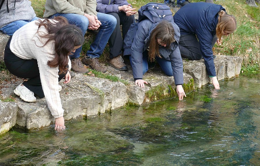 Drei Personen hocken am Gewässerrand und fassen ins Wasser
