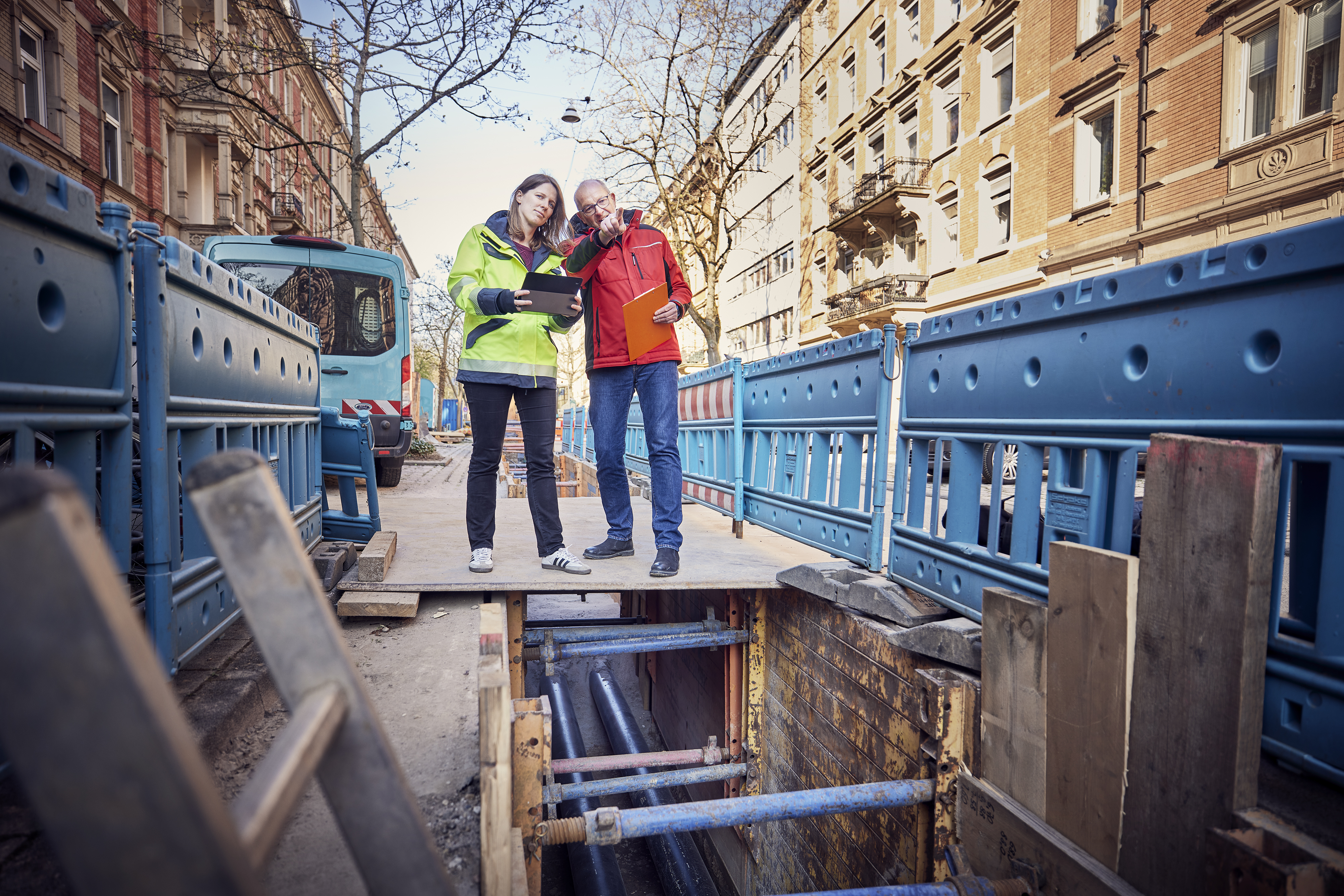 Mann und Frau stehen am Rande einer Fernwärmebaustelle und beraten sich.