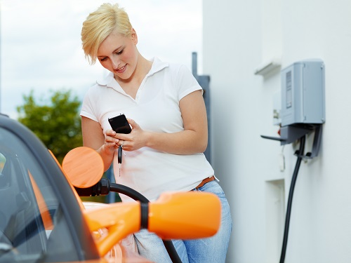 Frau mit Handy in der Hand lädt ein E-Auto