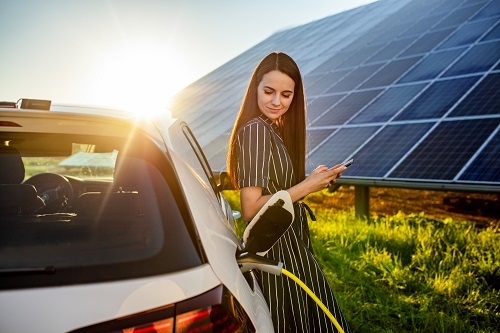 Frau lädt E-Auto vor PV-Anlage