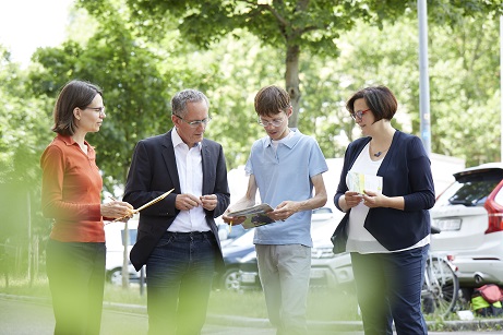 Das Bild zeigt vier Menschen, die konzentriert auf eine Zeitung oder ein Tablet schauen.uen